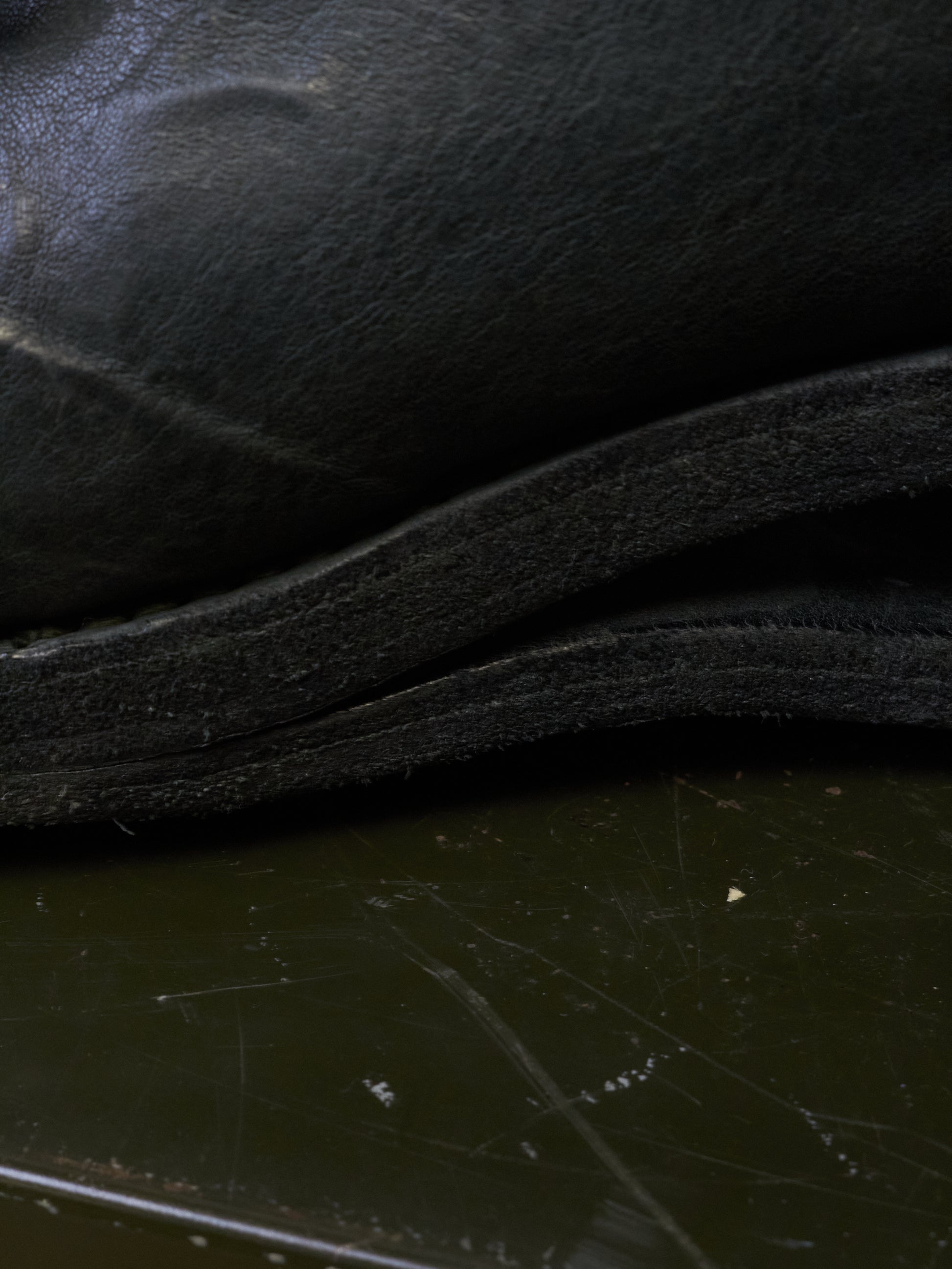 Close-up detail of a black leather or faux-leather item, showing layered edges and a dark reflective surface below.