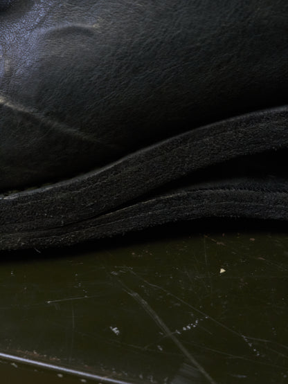 Close-up detail of a black leather or faux-leather item, showing layered edges and a dark reflective surface below.