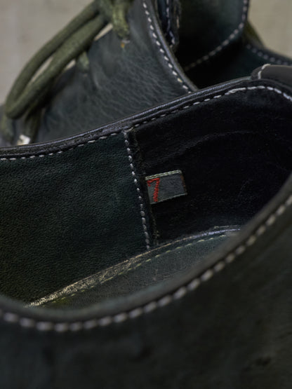Close-up detail of a dark leather shoe showing the interior lining, white contrast stitching, and a small red embroidered size marker.