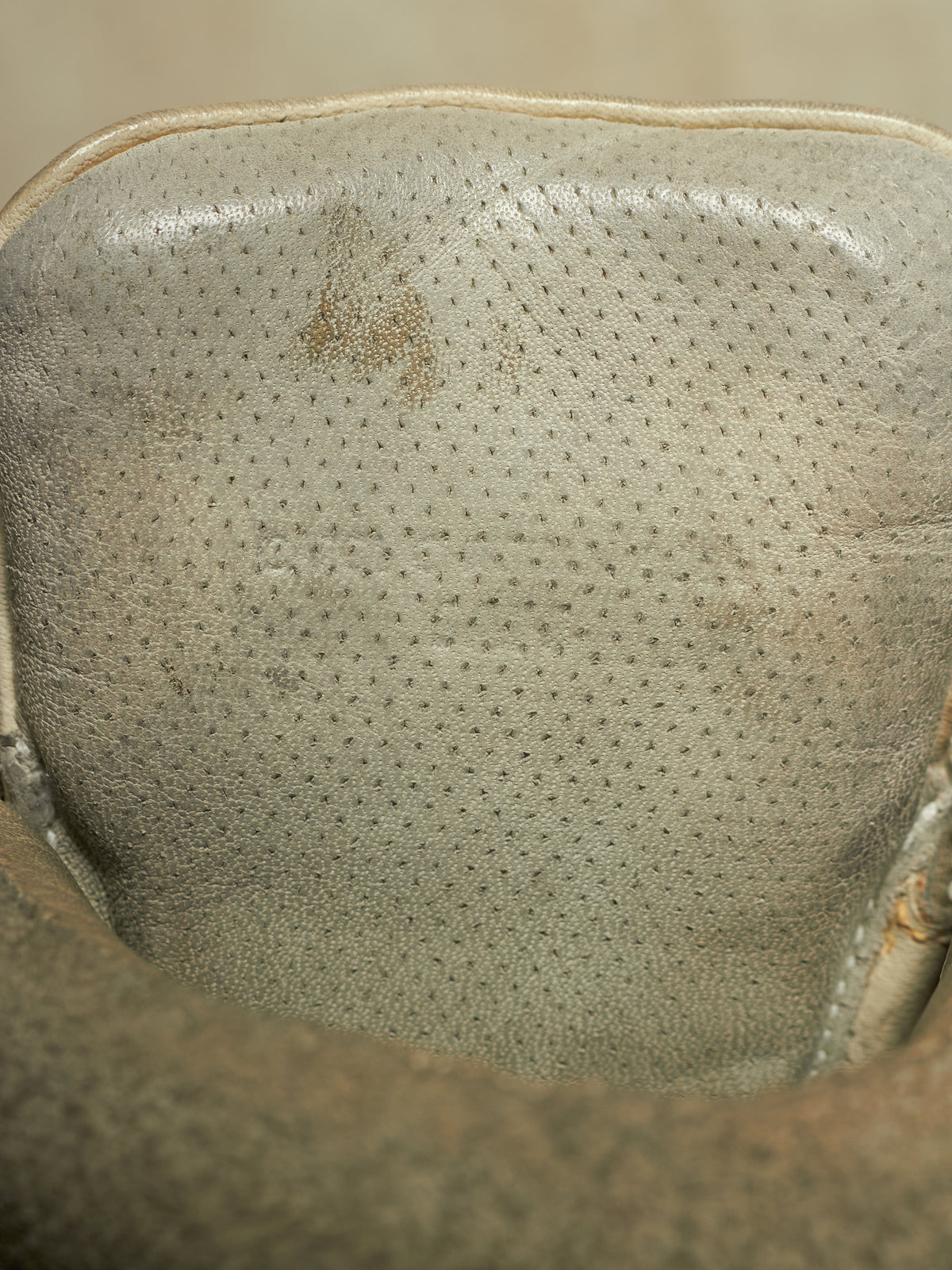 Close-up of the interior collar of a light beige leather shoe or boot, showing a perforated texture and a small brown stain.