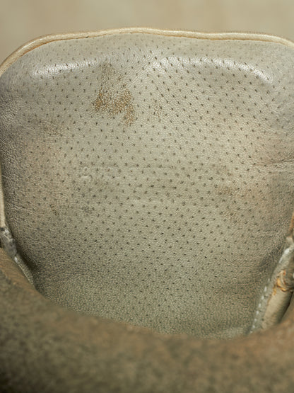 Close-up of the interior collar of a light beige leather shoe or boot, showing a perforated texture and a small brown stain.