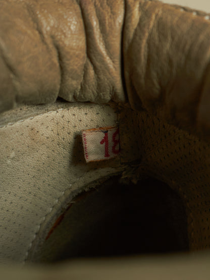 Close-up of the interior opening of a worn tan leather shoe or boot, showing textured leather, stitching, a small fabric tag with red numbering, and a dark shadowed interior.