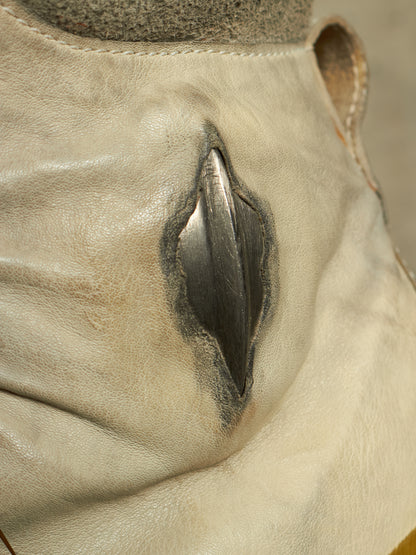 Close-up of a light beige leather boot or shoe with a prominent dark metallic rivet on the side.