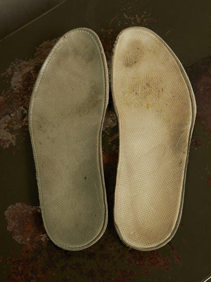 A pair of used, worn-in orthopedic shoe insoles displayed side-by-side on a dark, rusty metal surface.