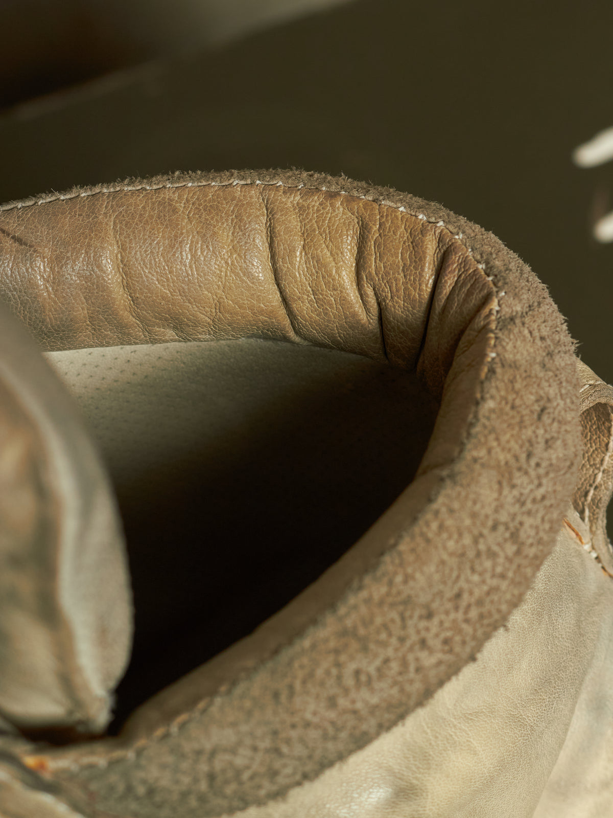 Close-up detail of a worn leather boot collar showing the tan leather trim, stitching, and interior lining.