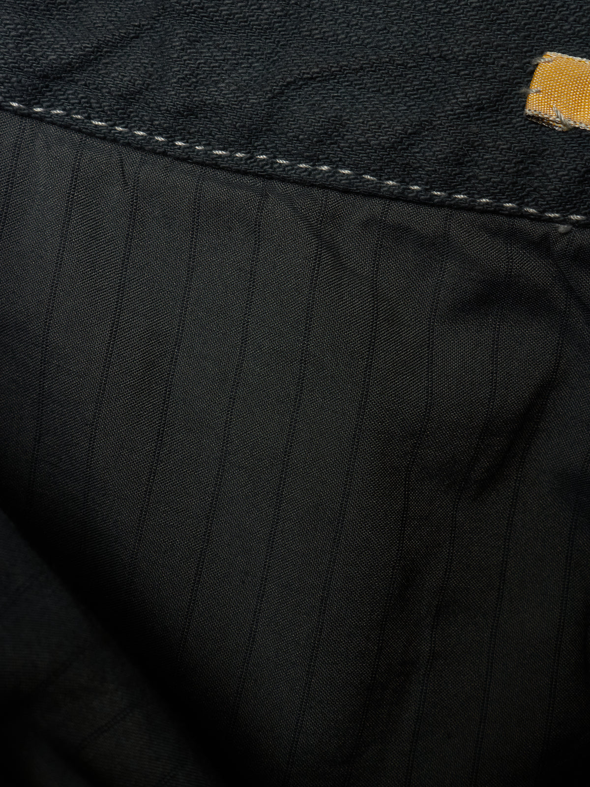 Close-up detail of black pinstriped fabric with contrast stitching and a small yellow brand tab.