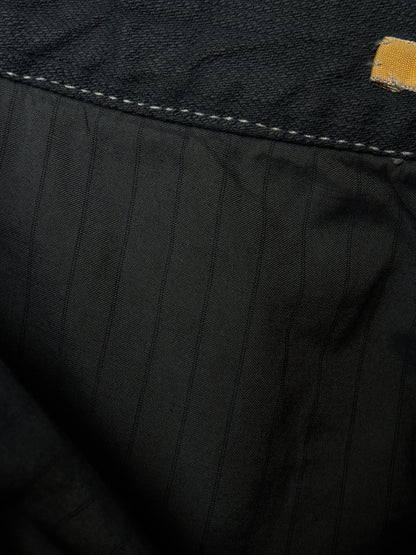 Close-up detail of black pinstriped fabric with contrast stitching and a small yellow brand tab.