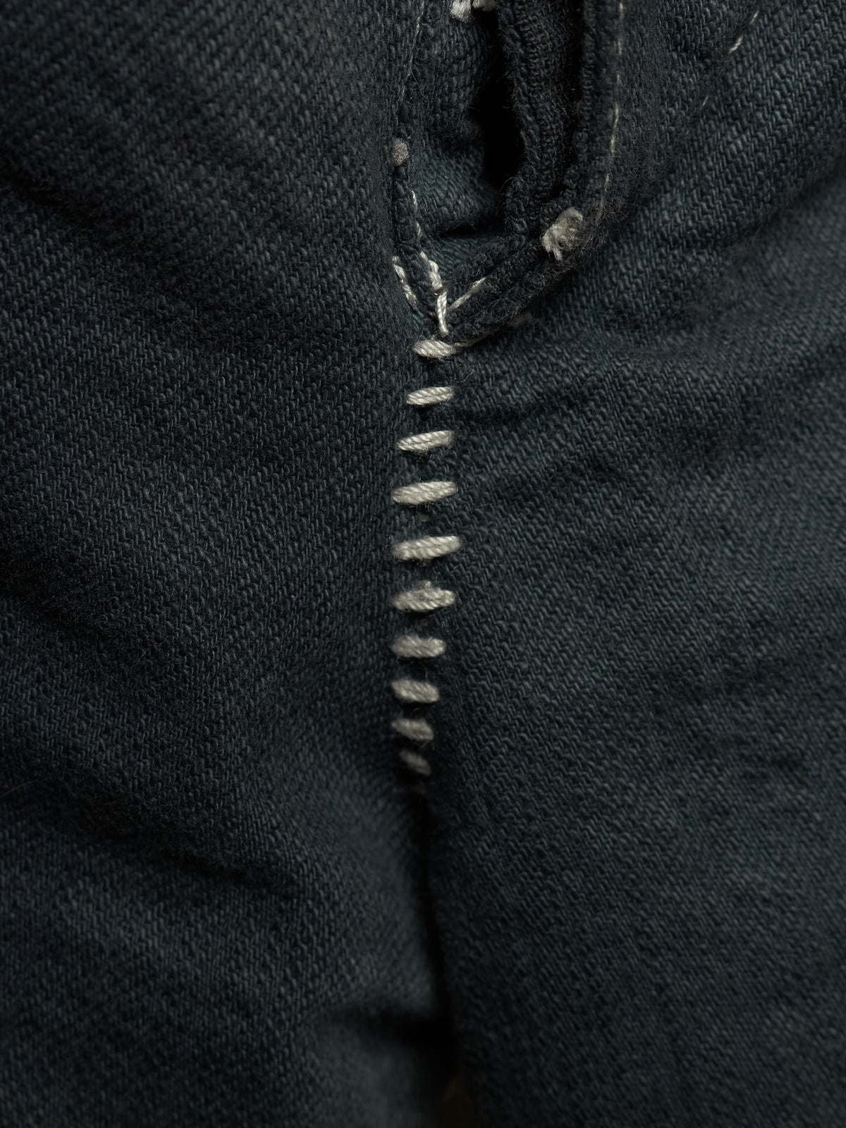 Close-up of dark indigo denim fabric with a vertical row of light gray whipstitching.