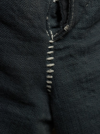 Close-up of dark indigo denim fabric with a vertical row of light gray whipstitching.