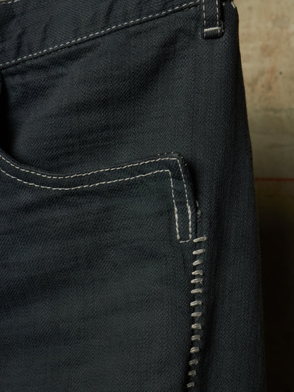 Close-up of the back pocket of dark indigo denim jeans, showing white contrast stitching and the texture of the denim fabric.