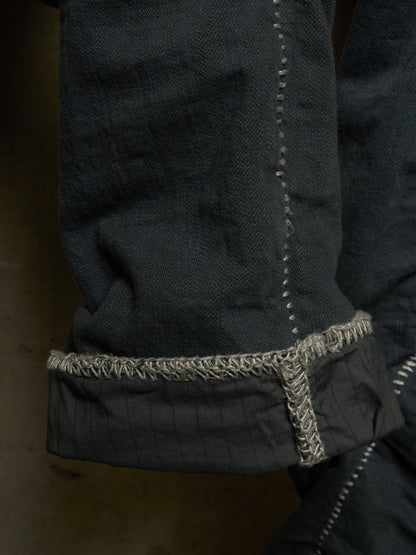 Close-up detail of a dark charcoal gray denim garment, showing a rolled cuff with contrasting light gray frayed stitching.