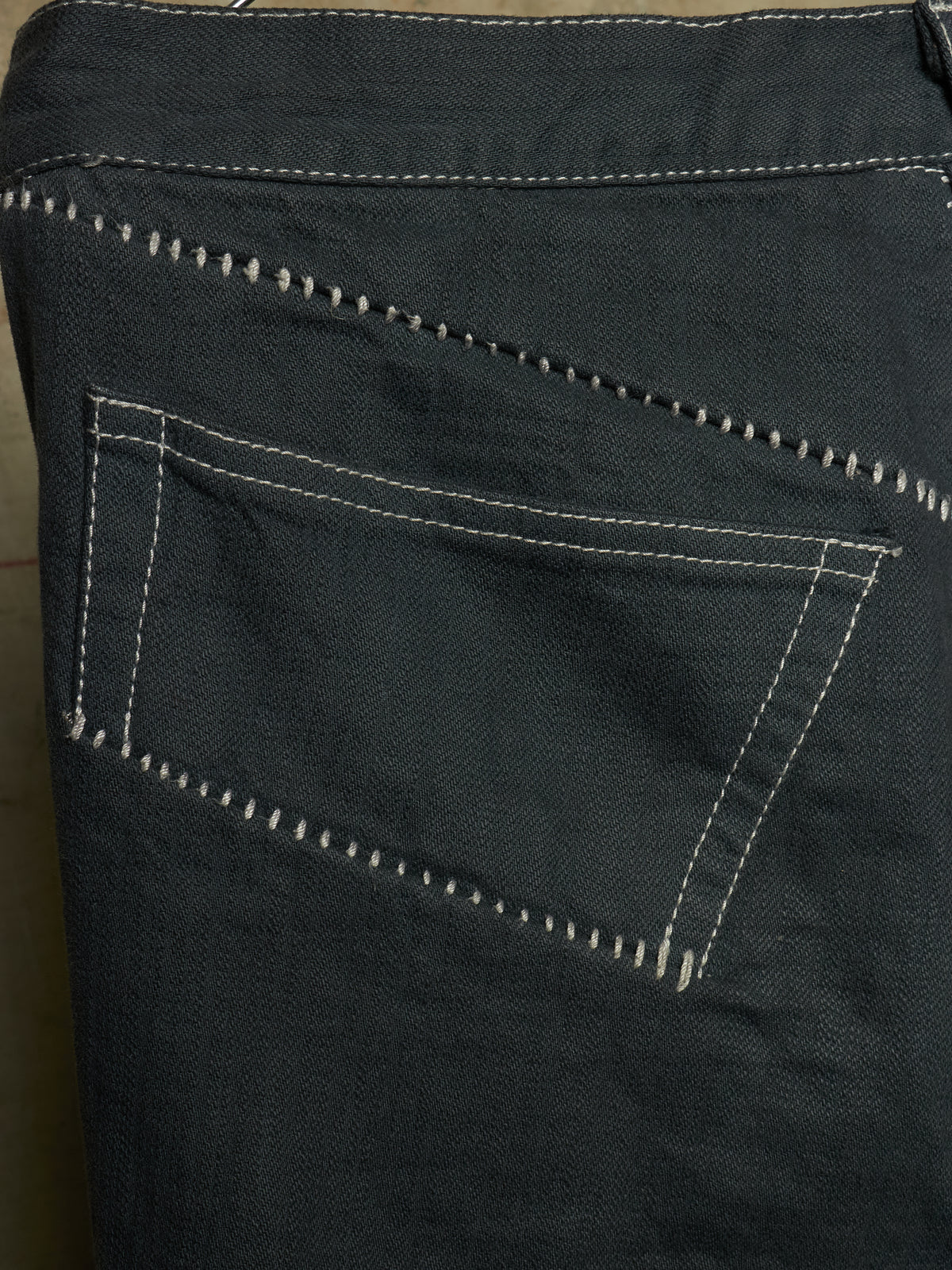 Close-up of the back pocket of dark charcoal gray denim jeans, showing white contrast stitching.