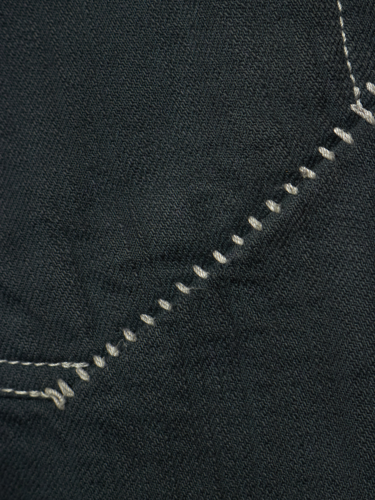 Close-up of dark charcoal gray denim fabric with white contrast stitching along a diagonal seam.