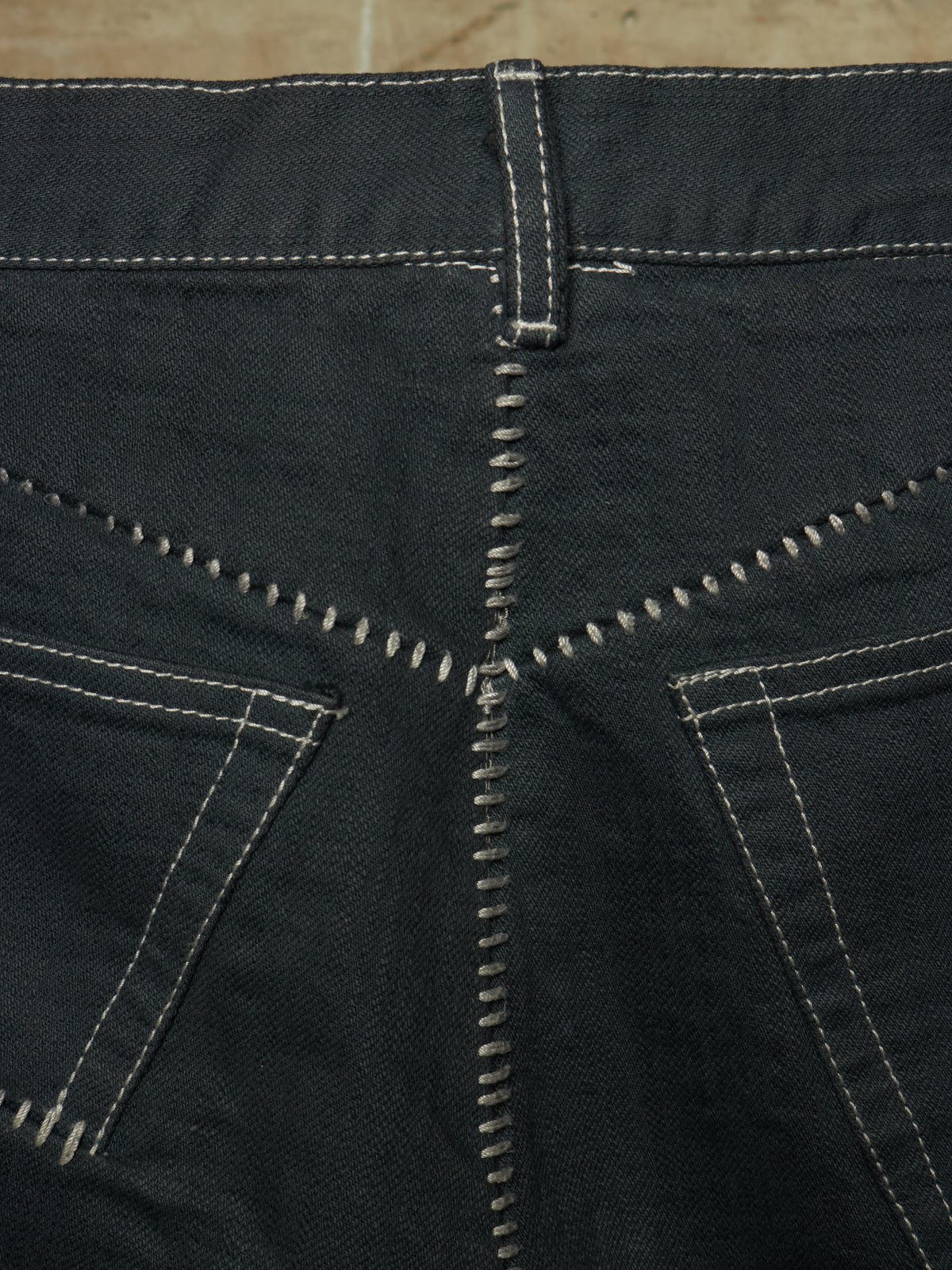 Close-up of the back waistband and pocket area of dark charcoal gray denim jeans, showing contrast white stitching details.