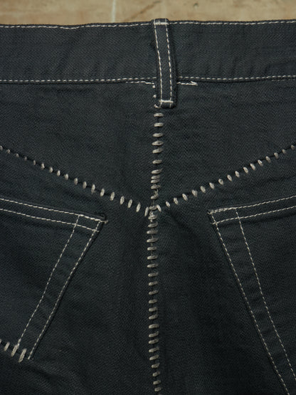 Close-up of the back waistband and pocket area of dark charcoal gray denim jeans, showing contrast white stitching details.