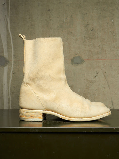 A single off-white leather ankle boot with a low stacked block heel, shown in profile on a dark reflective surface against a textured concrete wall.