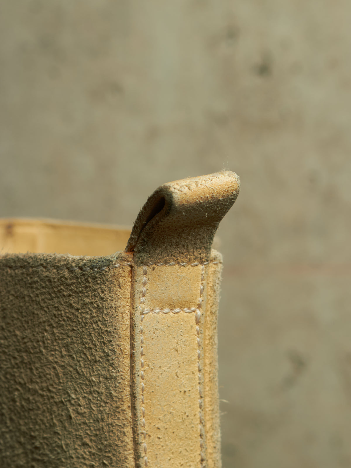 Close-up of a light tan suede or nubuck leather boot corner with a stitched pull tab, set against a textured concrete background.