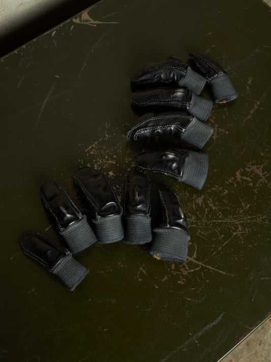 Six miniature black toy boots with gray ribbed cuffs, arranged on a dark green scratched tabletop.