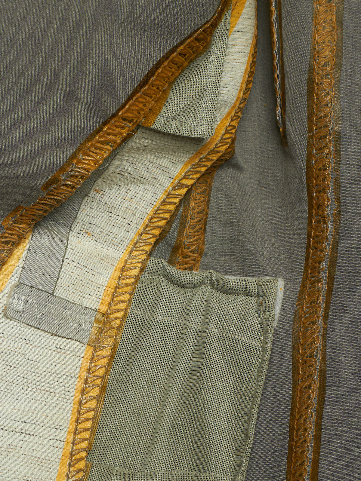 Close-up of a textured gray garment with decorative gold and beige embroidered trim and a matching fabric pocket.