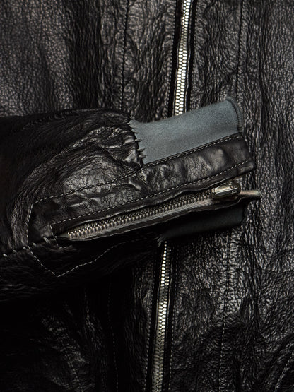 Close-up of a black leather jacket with a prominent front zipper, a zippered pocket on the sleeve, and a contrasting dark gray fabric lining.