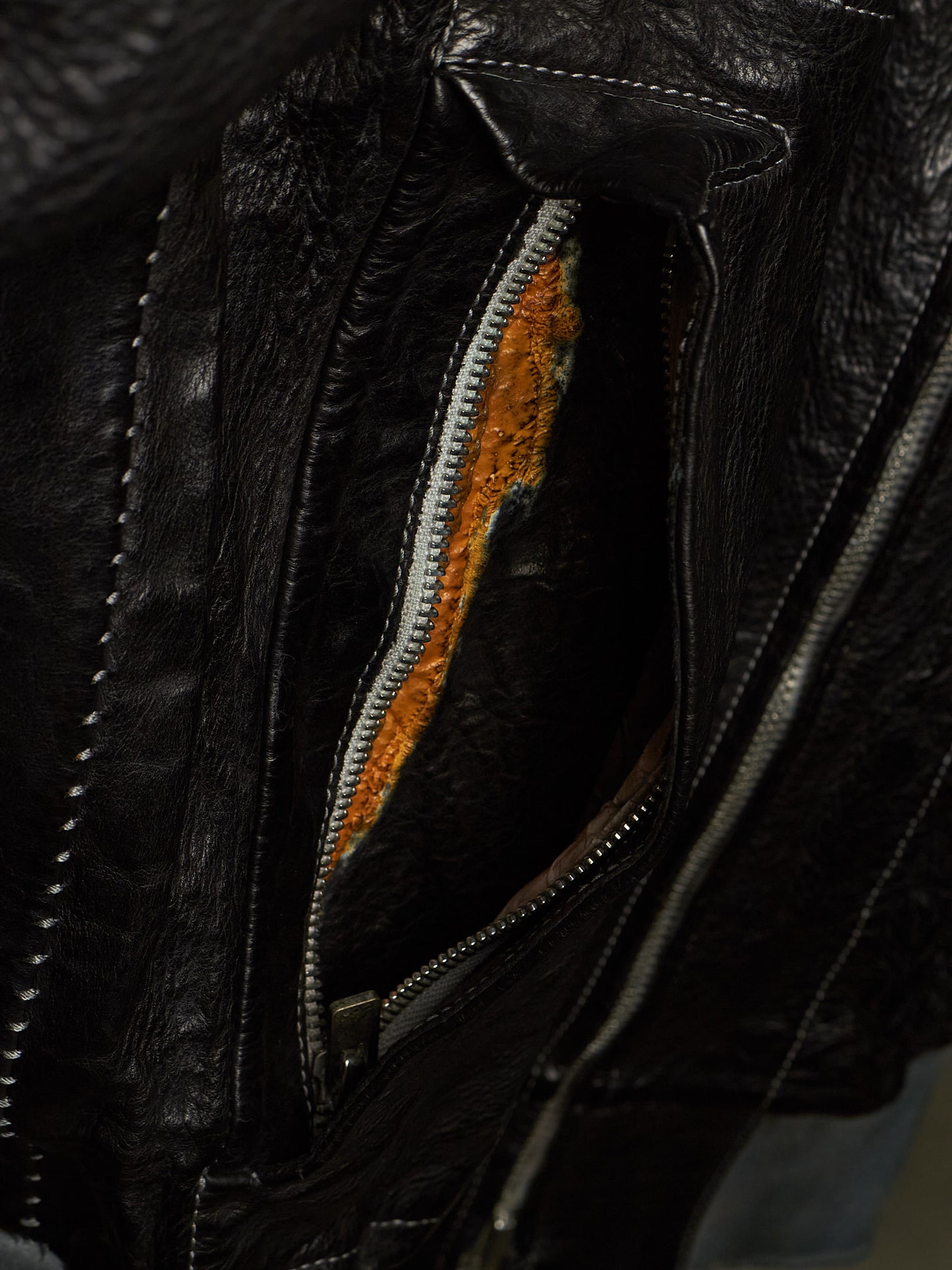 Close-up of a black leather jacket showing a zippered pocket with a textured orange lining.