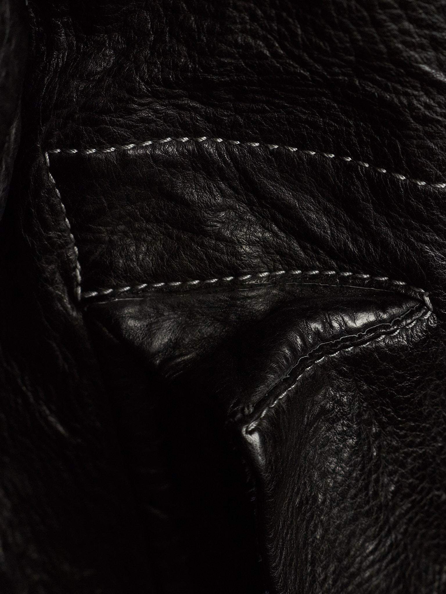 Close-up of a black leather jacket showing the texture of the leather and white contrast stitching.