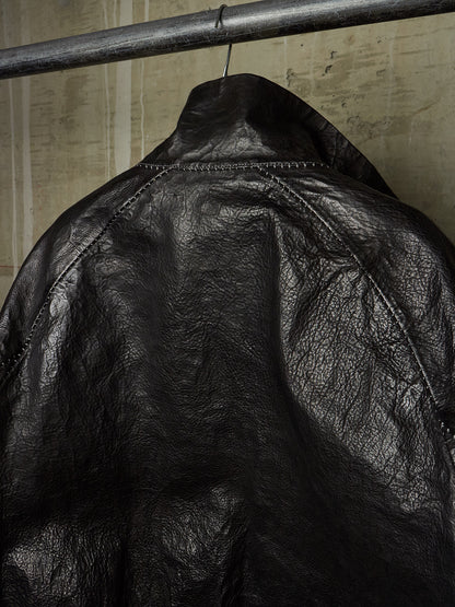 Close-up of a black leather jacket hanging on a metal clothing rack against a textured beige wall.