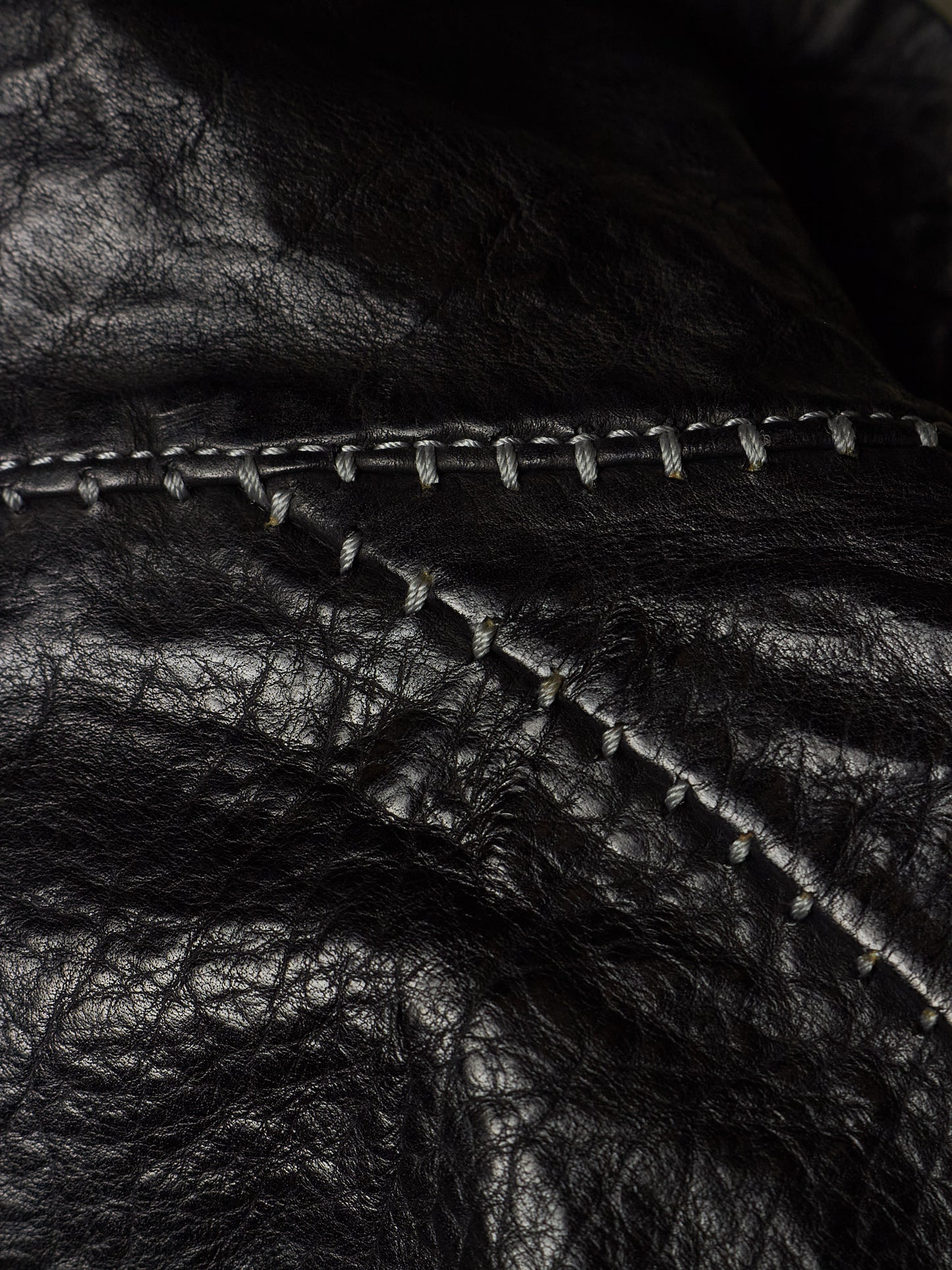 Close-up of black leather material with visible texture and contrast stitching along a curved seam.