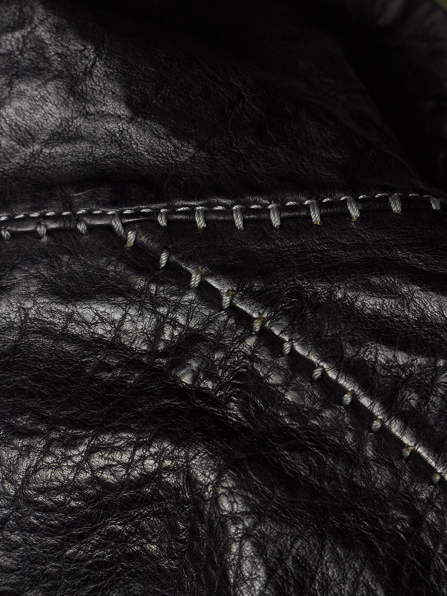 Close-up of black leather material with visible texture and contrast stitching along a curved seam.
