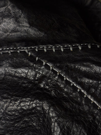 Close-up of black leather material with visible texture and contrast stitching along a curved seam.