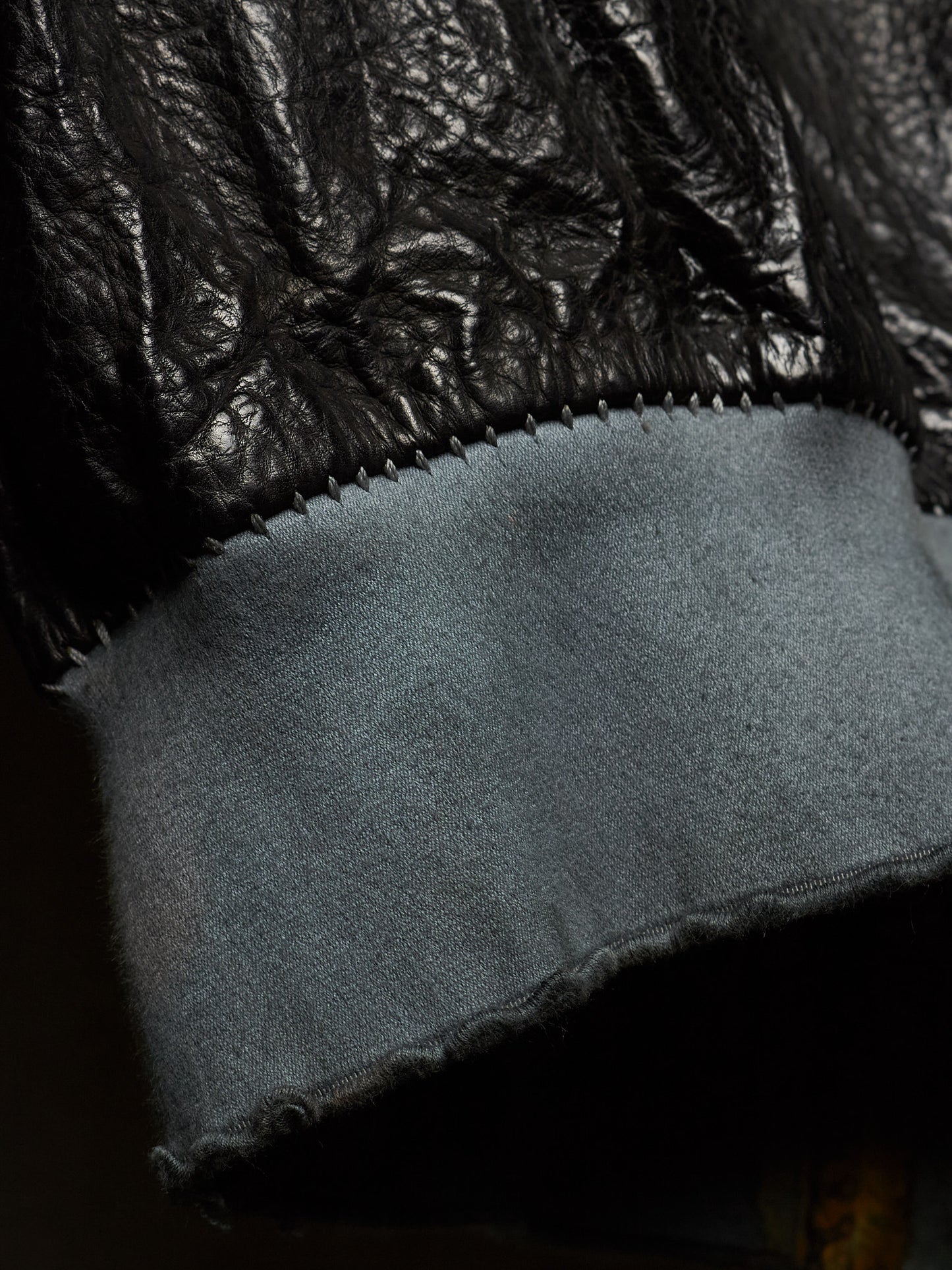 Close-up detail of a black leather jacket cuff with a wide, frayed light blue-gray suede or wool lining.