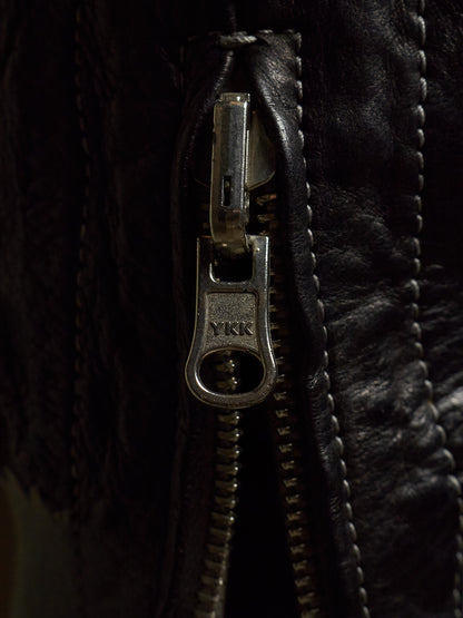 Close-up of a black leather jacket featuring a silver metal zipper with a pull tab engraved with the YKK logo.