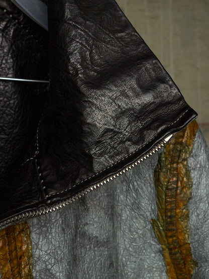 Close-up detail of a black leather jacket with a silver zipper, showing the texture of the leather and a portion of a gray and orange patterned garment underneath.