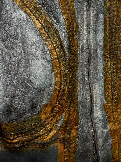 Close-up of a textured leather garment, showing a mix of metallic silver and warm golden-brown pebbled leather panels with a vertical zipper.