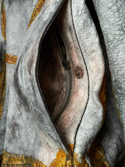 Close-up of a distressed leather jacket with a silver metal zipper and a brown snap button, showing the textured interior lining.