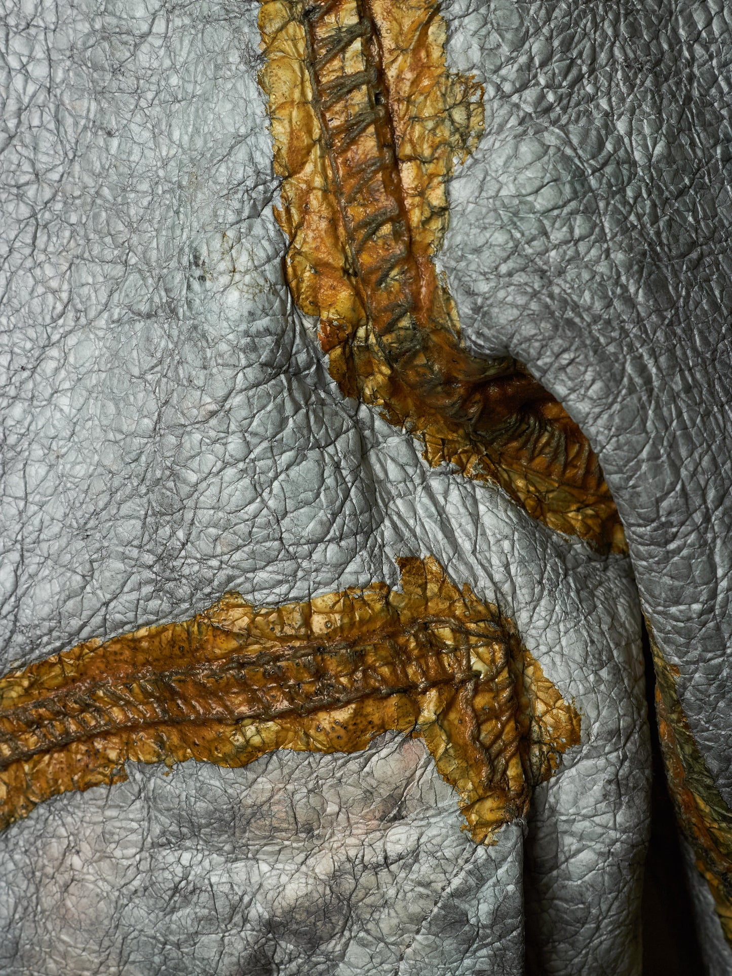 Close-up of textured gray leather with prominent distressed orange-brown stitched patches and seams.
