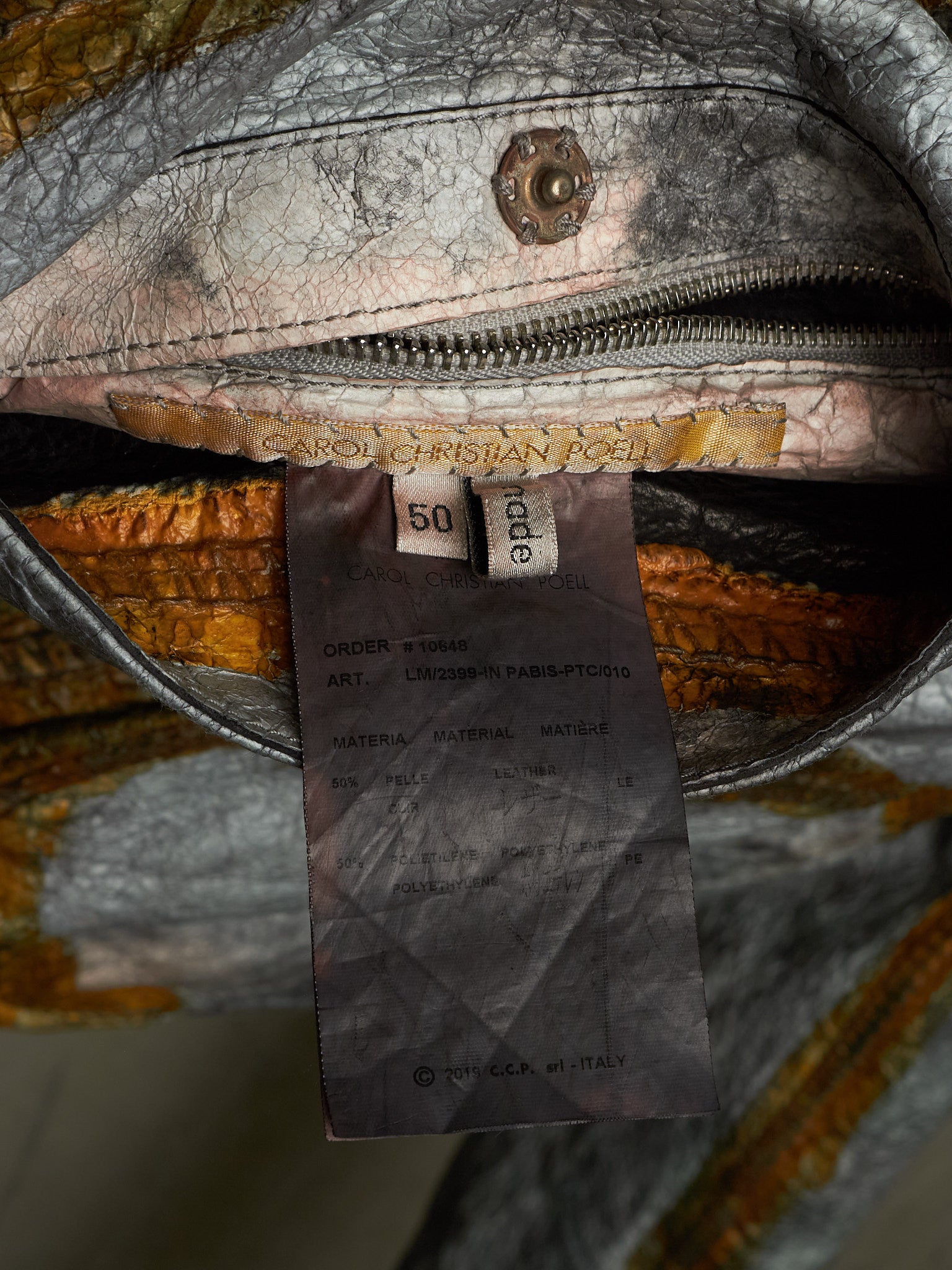 Close-up of the interior of a textured leather bag showing a zipper, interior lining, a sewn-in size tag reading 50, and a paper brand tag for Carol Christian Feen.