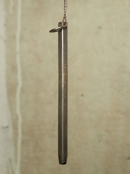 A vintage silver-toned metal bullet pendant hanging from a chain against a textured beige background.