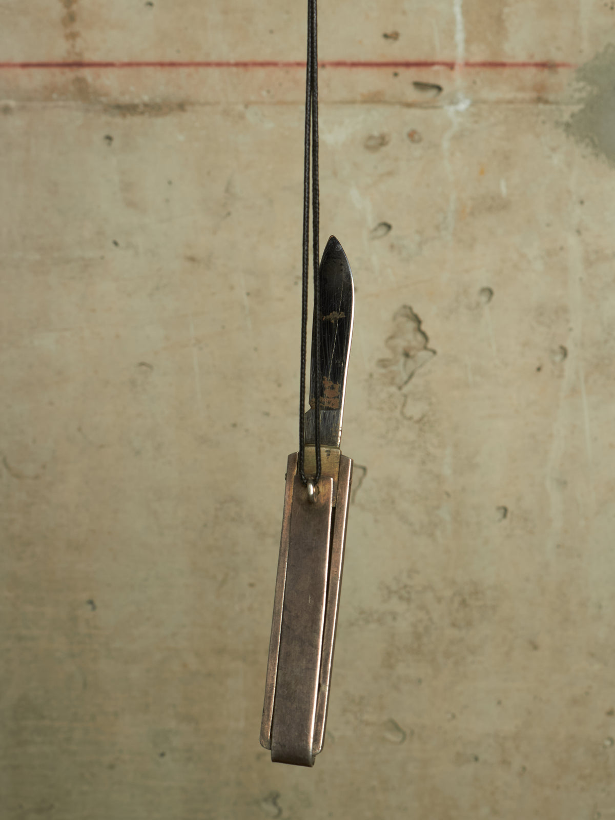 A vintage folding pocket knife with a dark steel blade and a bronze-toned metal handle, suspended vertically against a textured beige background.