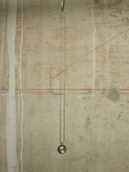 A silver metal chain pull-down faucet fixture hanging from a metal rod against a textured beige concrete wall.