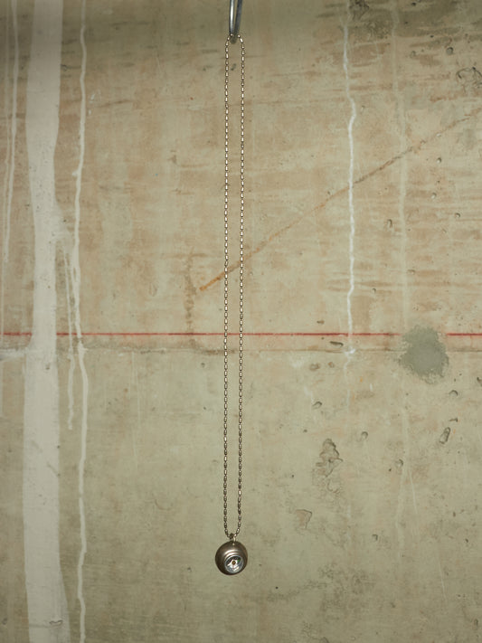 A silver metal chain pull-down faucet fixture hanging from a metal rod against a textured beige concrete wall.