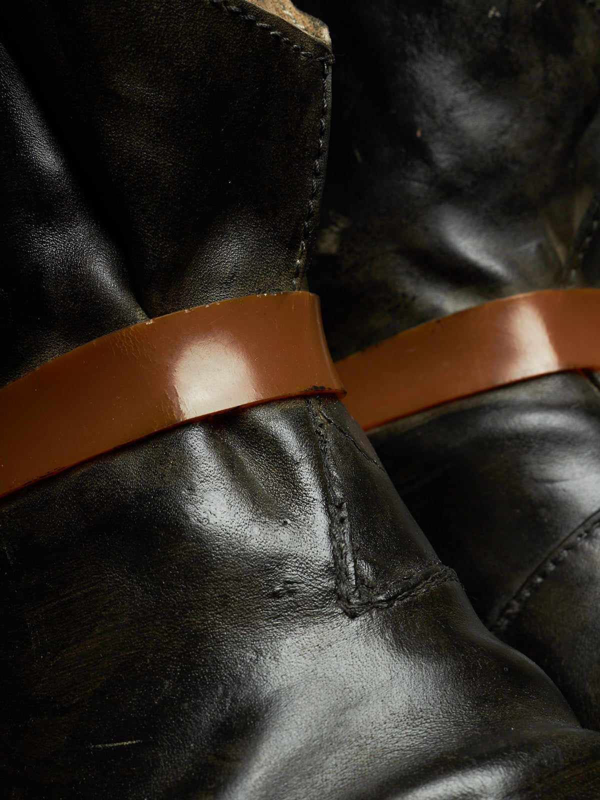 Close-up of black leather boots with a smooth brown leather strap detail around the shaft.