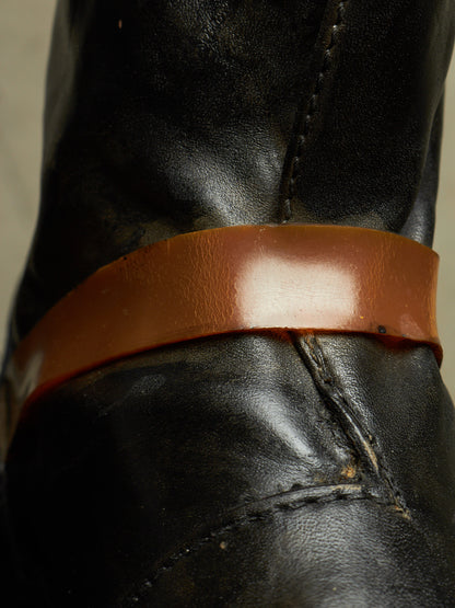 Close-up of a black leather boot with a wide, glossy brown leather band around the shaft.