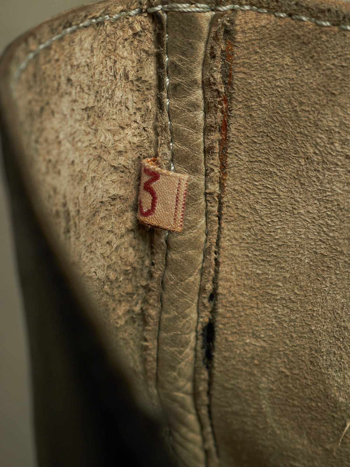 Close-up of a distressed brown leather boot showing the interior lining, heavy stitching, and a small fabric tag with the number 3.