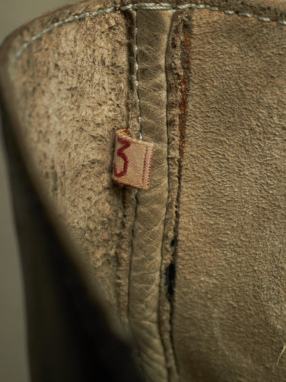 Close-up of a distressed brown leather boot showing the interior lining, heavy stitching, and a small fabric tag with the number 3.
