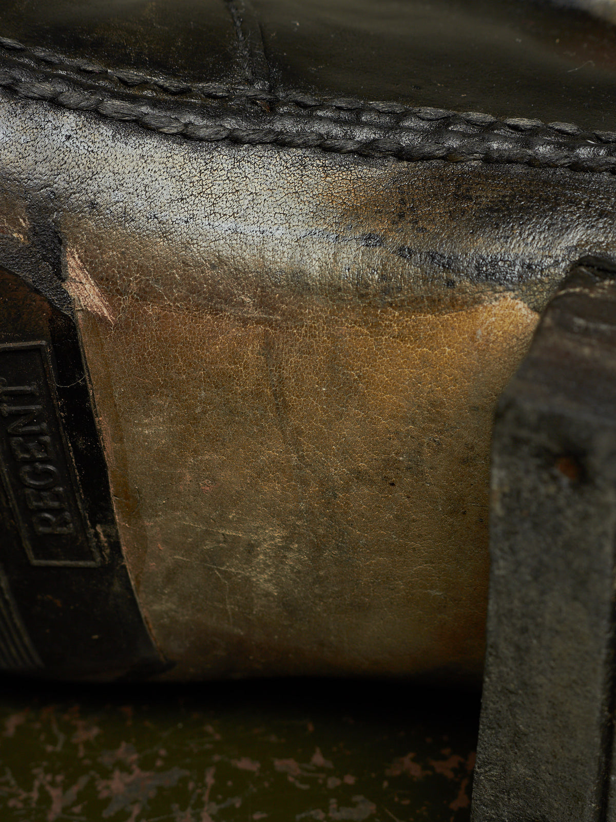 Extreme close-up of a worn leather boot or shoe sole showing a heavily scuffed, stained surface with a black rubber outsole and a partially visible 'REGENT' brand tab.