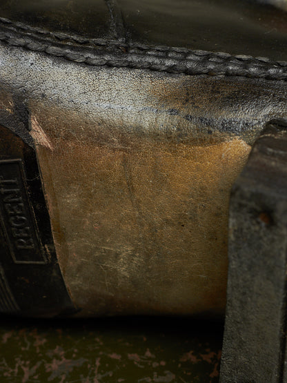 Extreme close-up of a worn leather boot or shoe sole showing a heavily scuffed, stained surface with a black rubber outsole and a partially visible 'REGENT' brand tab.