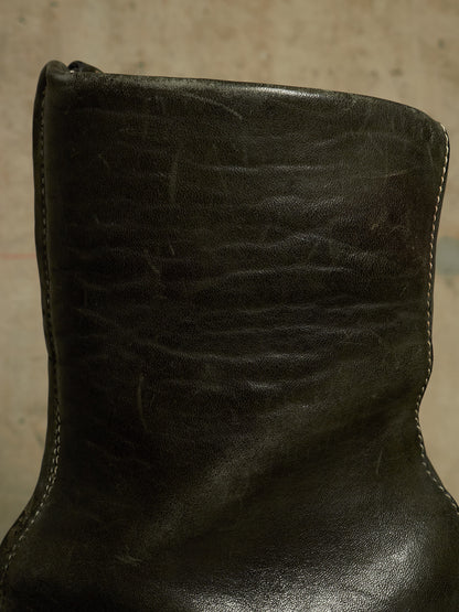 A close-up of a dark olive green leather boot showing the textured leather surface, stitching, and a portion of the sole.