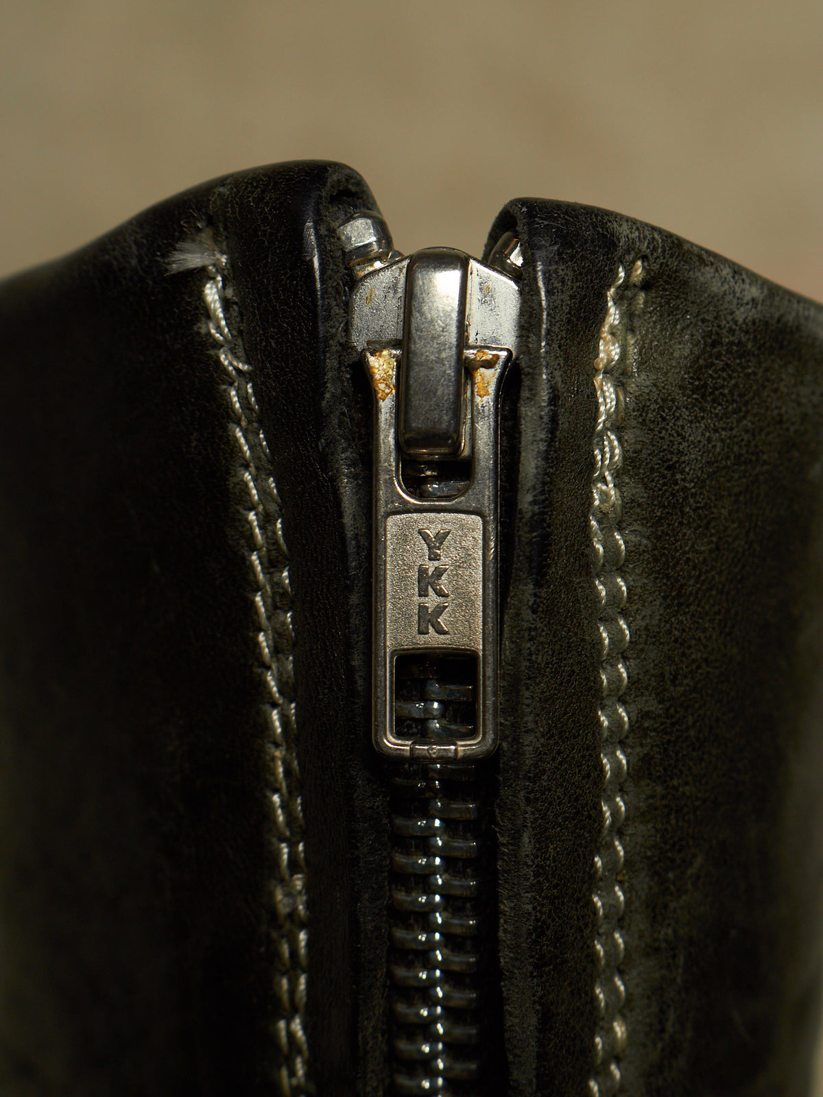 Close-up of a black leather zipper with a silver metal pull tab engraved with the letters 'YKK'.