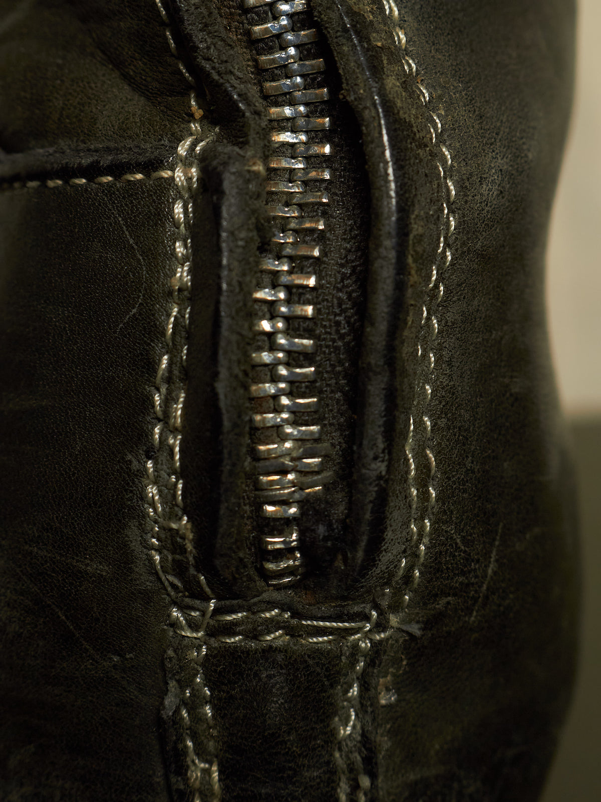 Close-up of a black leather zipper detail with contrast stitching on a dark leather item.